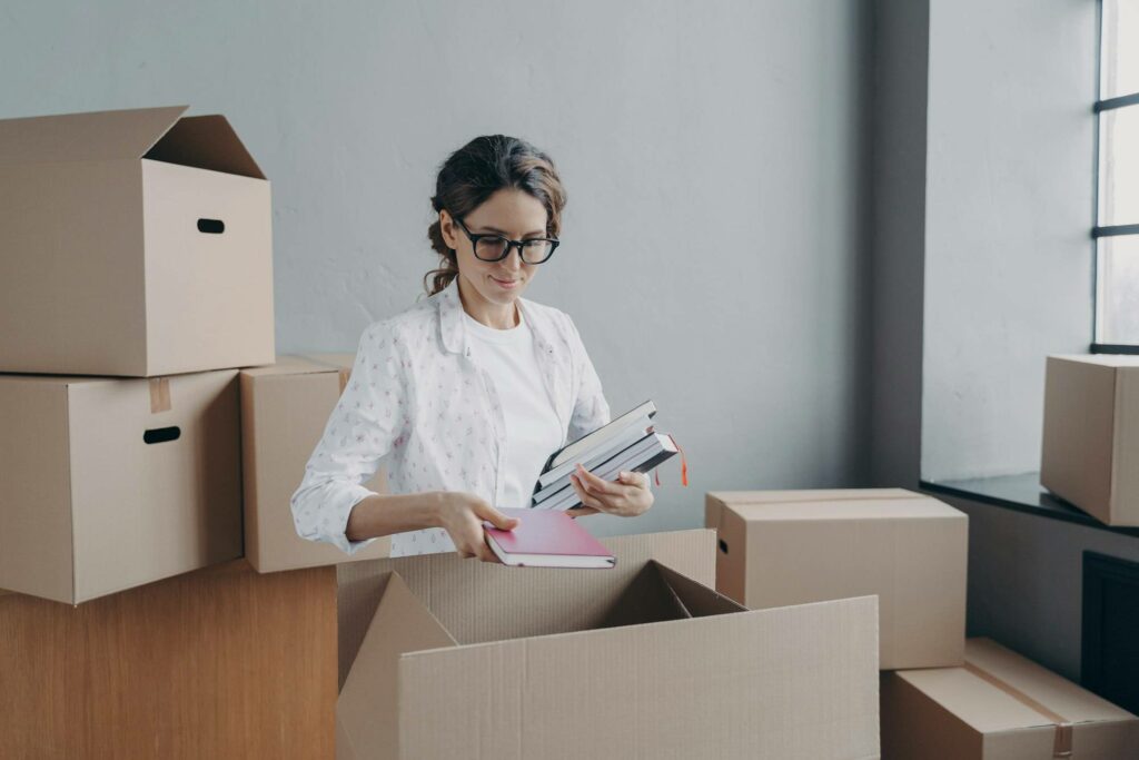 Femme triant des documents et livres près de cartons, contexte déménagement entreprise, check list déménagement entreprise etude.