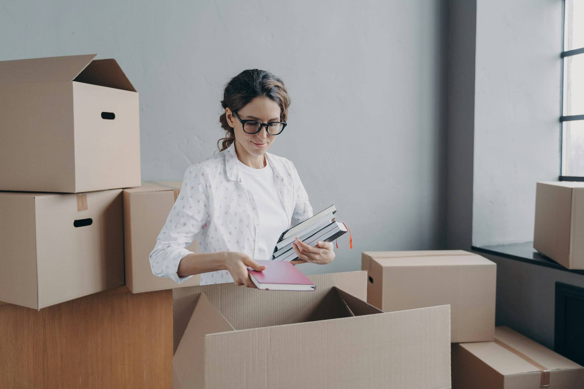 Femme devant des cartonnettes et boîtes, tenant des dossiers et des carnets; déménagement de bureaux et démarches administratives déménagement bureau.