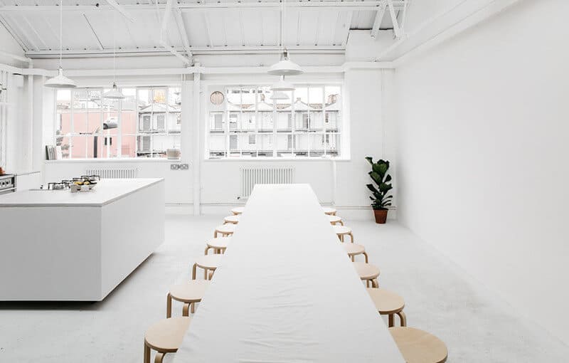 Salle blanche épurée avec long table et chaises en bois autour; espace lumineux prêt pour réunion, cuisine à gauche. 14 choses à jeter en un jour pour être mieux