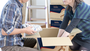 Deux personnes déballent des cartons dans une pièce remplie d’emballages et de boîtes.