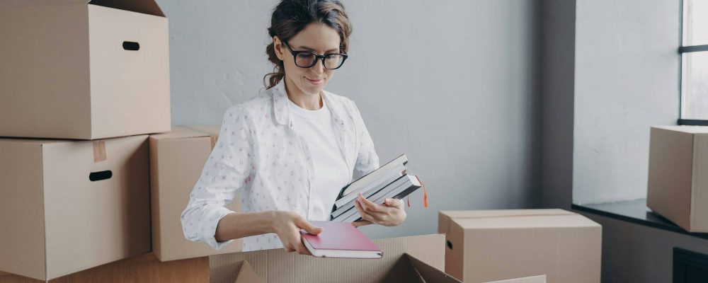 Femme devant des cartonnettes et boîtes, tenant des dossiers et des carnets; déménagement de bureaux et démarches administratives déménagement bureau.